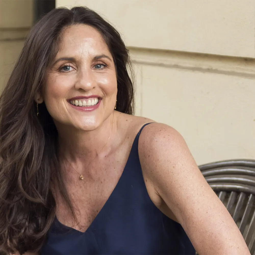 Sarah Gale laughing in a navy camisole beside a cane chair
